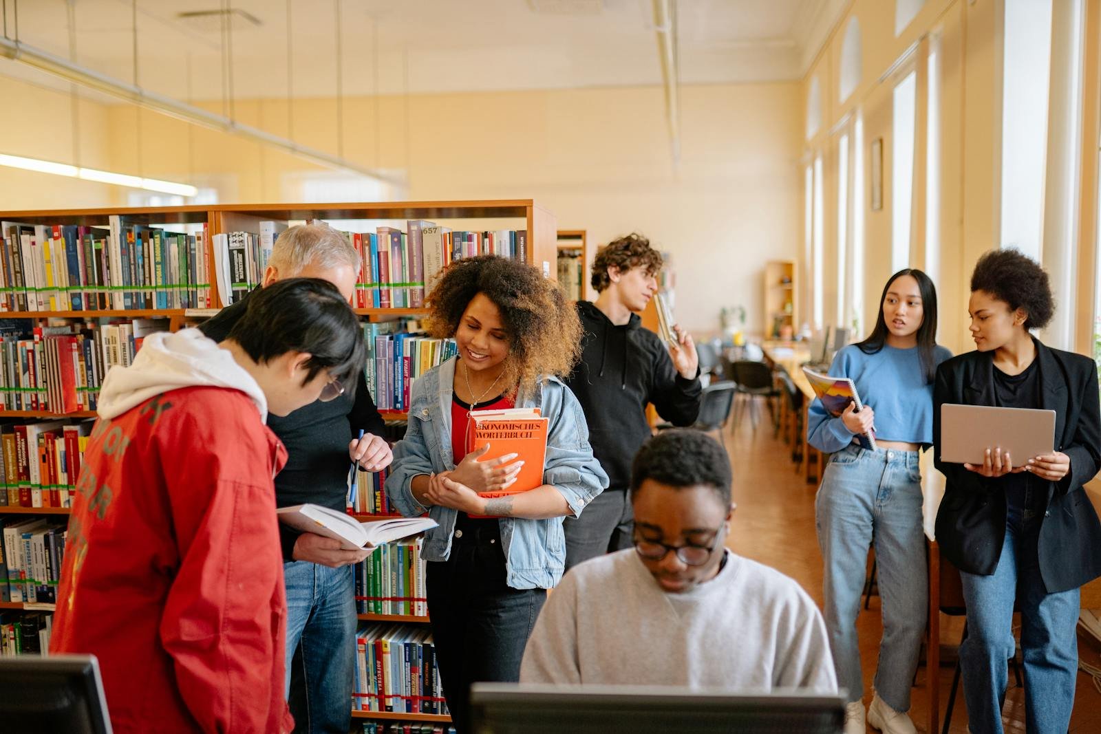 A diverse group of students studying together at a university library, engaging with books and technology.