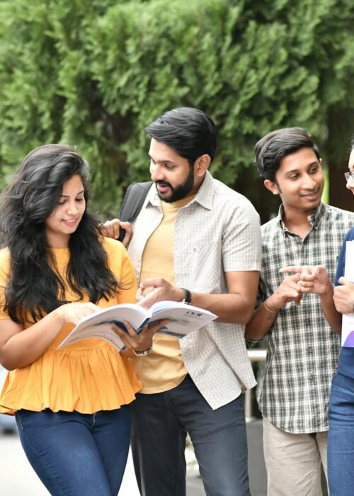A group of diverse college students engaged in outdoor group study session, sharing books and ideas.