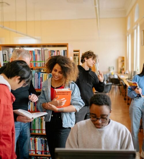 A diverse group of students studying together at a university library, engaging with books and technology.