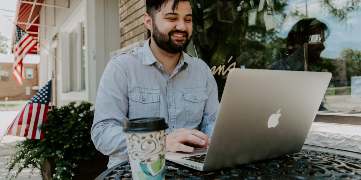 man in gray denim dress shirt smiling while using MacBook Pro